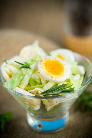 fresh spring salad with cabbage, lettuce and boiled eggs with rosemary and spices on a wooden tableの写真素材