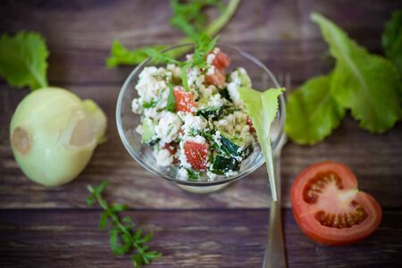 fresh cottage cheese salad with cucumbers and tomatoes with herbs in a bowl on the tableの写真素材