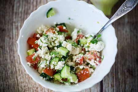 fresh cottage cheese salad with cucumbers and tomatoes with herbs in a bowl on the tableの写真素材