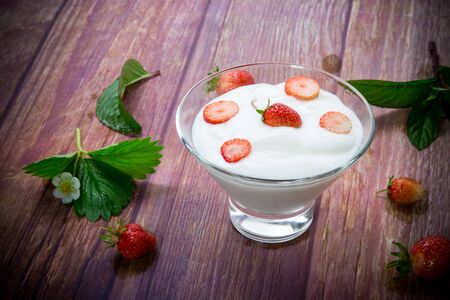 sweet homemade yogurt with red ripe fresh strawberries in a glass bowl on a wooden tableの写真素材