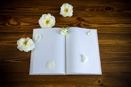 bouquet of beautiful white roses and blank notebook on a wooden table