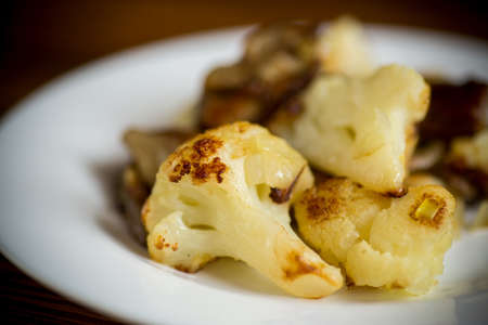 fried cauliflower with wild porcini mushrooms and onions in a plate, on a wooden table.の写真素材