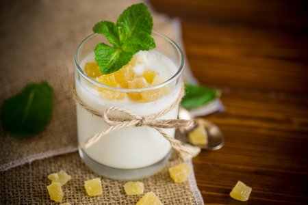 Sweet homemade yogurt with candied fruits in a glass on a wooden table.の写真素材