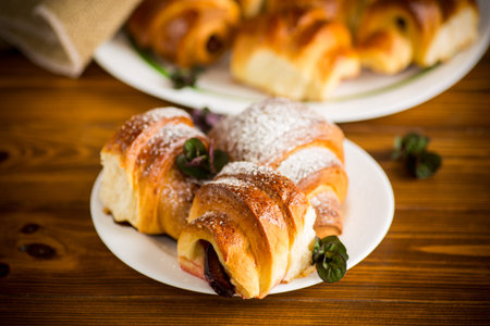 baked sweet homemade buns with plum inside, on a wooden table.