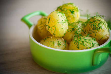 boiled early potatoes with butter and fresh dill in a bowl on a wooden tableの写真素材