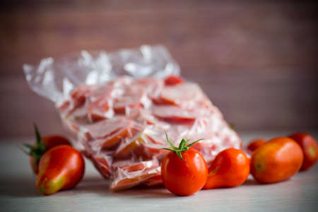 frozen tomatoes in a vacuum bag on a wooden tableの写真素材