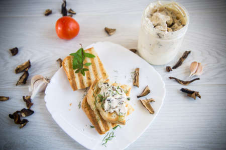 fried bread toast with cheese spread with boiled dried mushrooms, in a plate on a wooden table.の写真素材