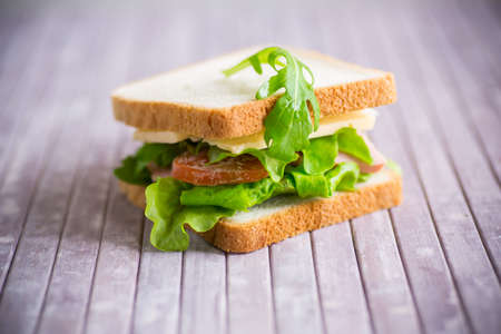 sandwich with various greens, cheese, sausage, tomato on a wooden tableの写真素材