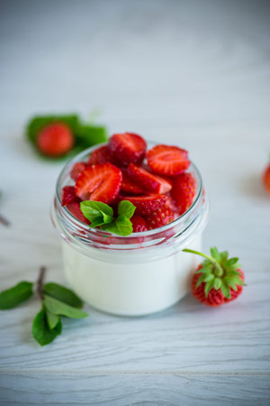 Sweet homemade yogurt with fresh ripe strawberries in a glass jar on a light wooden table