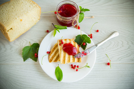 fried bread croutons for breakfast with redcurrant jam in a plate with berries on a wooden table.