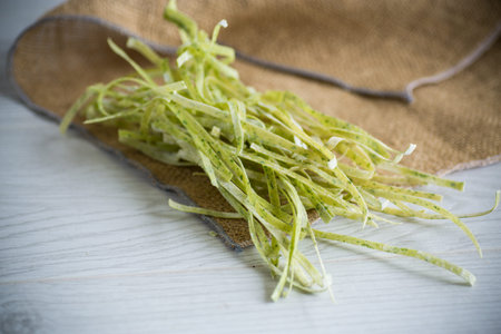 homemade dried green raw noodles with herbs on a wooden table