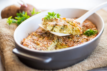 potato casserole with cabbage and spices in a ceramic form on a wooden table.の写真素材
