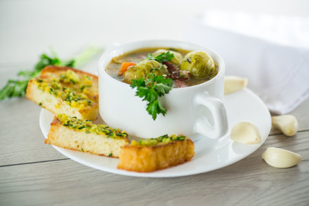 Hot cooked soup with Brussels sprouts, vegetables and croutons, in a plate on a wooden table.の写真素材