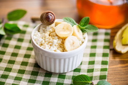 crumbly organic cottage cheese with honey and bananas in a ceramic bowl on the tableの写真素材