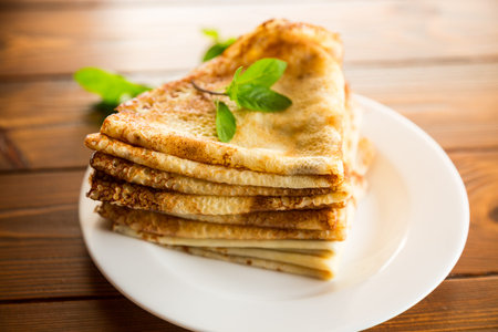 lot of thin pancakes in a plate, on a dark wooden table.