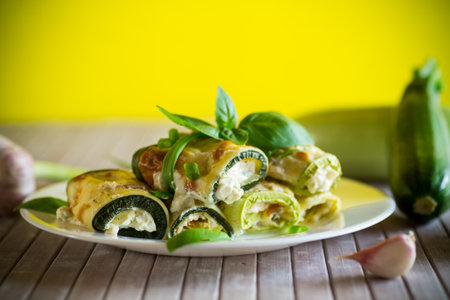 cooked zucchini rolls stuffed with cheese inside, in a plate on a green backgroundの写真素材