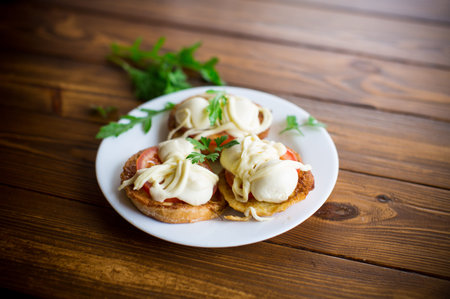 fried in batter sandwiches with tomatoes and mozzarella in a plate with herbs, on a wooden table.
