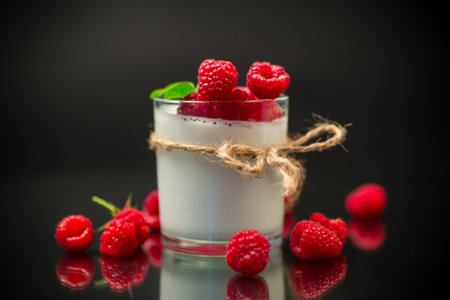 Cooked homemade yogurt with ripe red raspberries in a glass isolated on a black backgroundの写真素材