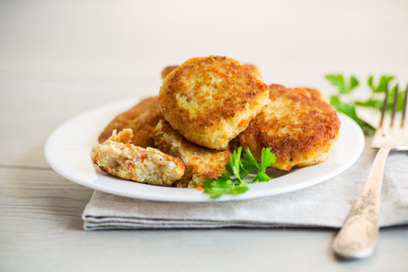 Cooked fried fish cutlets in a plate with herbs, on a light wooden table.の写真素材