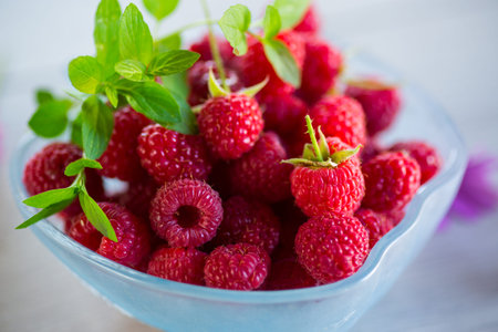 Fresh ripe raspberries in a glass bowl on a light wooden table.