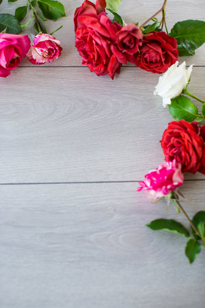 Floral background of pink, red and other roses on a light wooden tableの写真素材