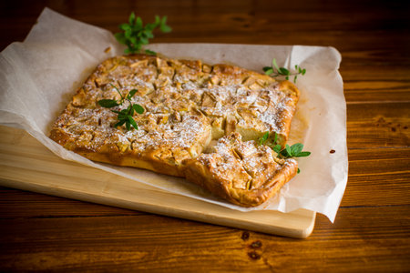 prepared curd semolina pie with quince inside and covered with powdered sugar on a wooden board.の写真素材