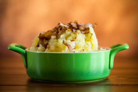 Cooked mashed potatoes with fried chopped bacon and onions in a bowl.