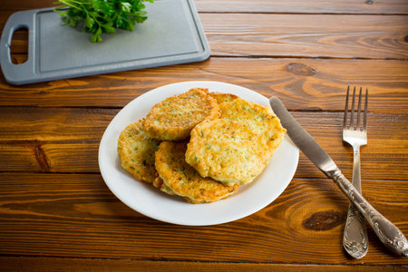 cooked fried potato cutlets with herbs, in a plate on a wooden table.