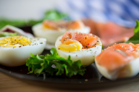 boiled eggs with salted red fish, herbs and seasonings in a plate on a wooden table.の写真素材