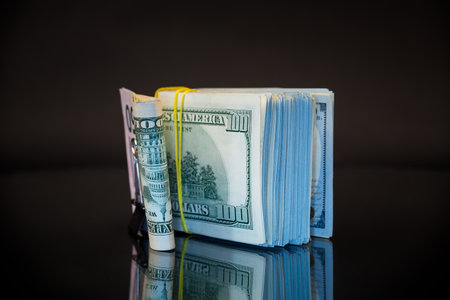 stack of dollar bills collected in an elastic band and a stationery clip, isolated on a black background.の写真素材