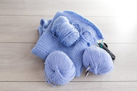 Hand knitting kit, blue yarn, knitting needles and more on a light wooden background.