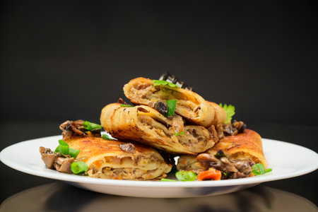 fried thin pancakes stuffed with meat, mushrooms, in a plate isolated on a black background.の写真素材