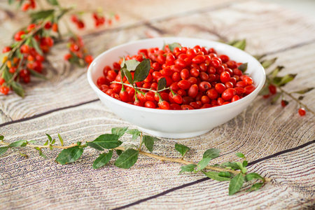 fresh ripe red goji berries in a bowl on a wooden table.