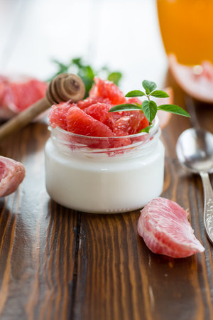 homemade sweet yogurt in a glass jar with pieces of red ripe grapefruit and honey, on a wooden table.の写真素材