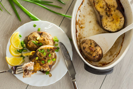 Homemade fish dish with lemon and herbs in a plate on a wooden table.
