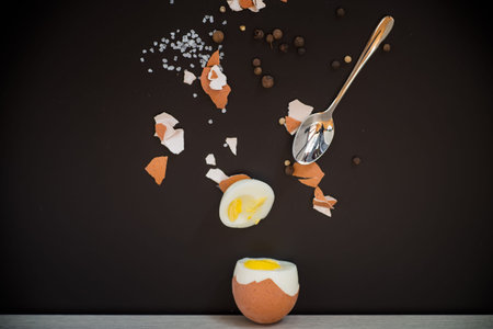 Boiled egg with spices and shell on black background.