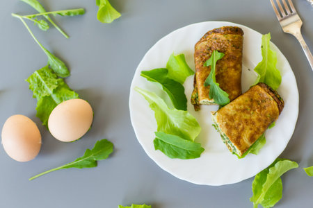 Omelette roll with greens and fresh arugula on a plate.