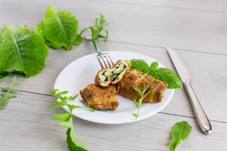 Omelette roll with greens on top on a wooden table.
