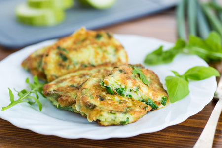 fried zucchini fritters with green onions in a plate on a wooden table.の写真素材