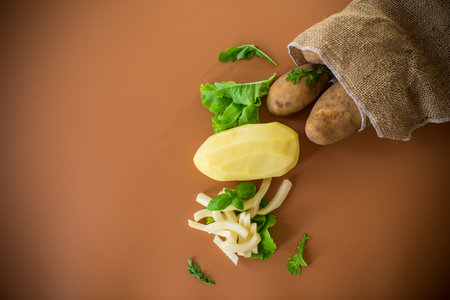 Root vegetable in a sack and sliced potatoes on a brown background.の写真素材