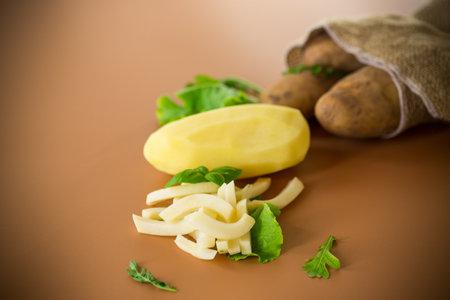 Still life with potatoes in a sack and slices on a brown background.の写真素材