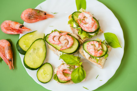 Small canapes with shrimps, salad and cucumbers on a green background.の写真素材