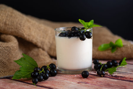 A glass of thick yogurt with currant berries for a healthy diet on a wooden.