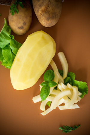 Raw peeled potatoes and slices on a brown background.の写真素材
