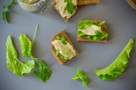 Slice of rye bread with cheese spread and greens on the table.