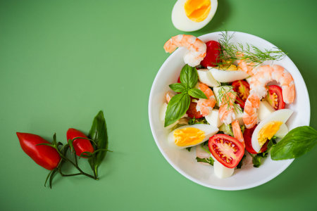Diet dish with shrimps, tomatoes and boiled eggs on a green background.