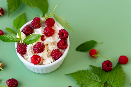 Cottage cheese with raspberries and green leaves on a green background.