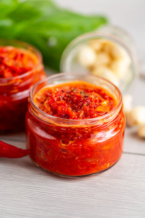 Bright red pepper condiment in jars with fresh ingredients.の写真素材