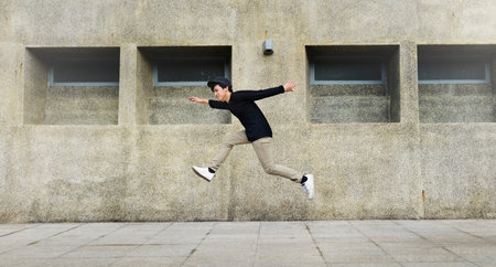Young man jumping in frount of university campus building