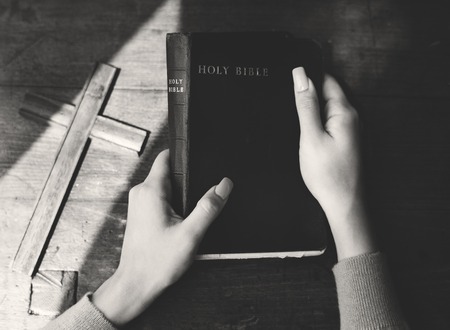 Hands Holding Holy Bible with Wooden Cross